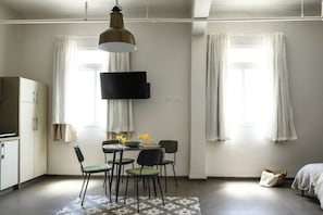 A compact room with a dining table, chairs, a flat-screen TV, and a bed. - The Printhouse Boutique Studio 5 by SeaNRent (Haifa)
