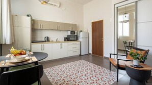 Eine moderne Küche mit weißen Schränken, einer Mikrowelle und einem Kühlschrank. Es gibt eine Essecke mit einem Tisch, Stühlen und einem gemusterten Teppich.