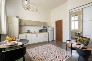 A modern kitchen with white cabinets, a microwave, and a refrigerator. There is a dining area with a table, chairs, and a patterned rug.