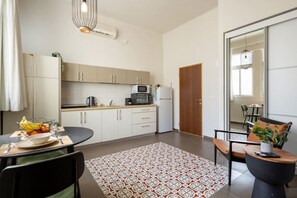 Eine moderne Küche mit weißen Schränken, einer Mikrowelle und einem Kühlschrank. Es gibt eine Essecke mit Tisch, Stühlen und einem gemusterten Teppich.