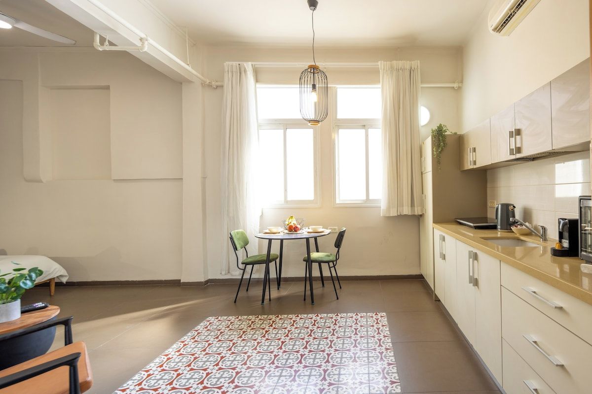 A compact kitchen with a dining area, a hanging light fixture, and a window with curtains.
