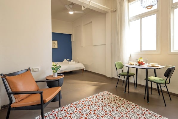 A hotel room with a bed, a small table with chairs, a window with curtains, and a decorative rug.