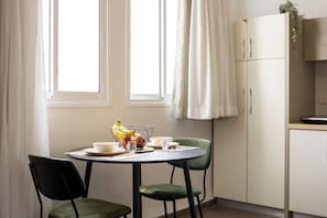 A dining area with a table set for two, a bowl of fruit, and a cabinet with a plant on top.