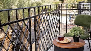A balcony with a metal railing, a green chair, a small table with a plate of cookies, a glass of red drink, and a potted plant.