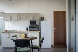 A compact kitchen with a microwave, toaster, and refrigerator. There is a dining table with chairs and a bowl of fruit.