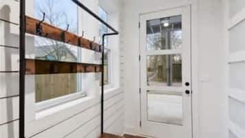 A hallway with a wooden bench, a white door, and a window.