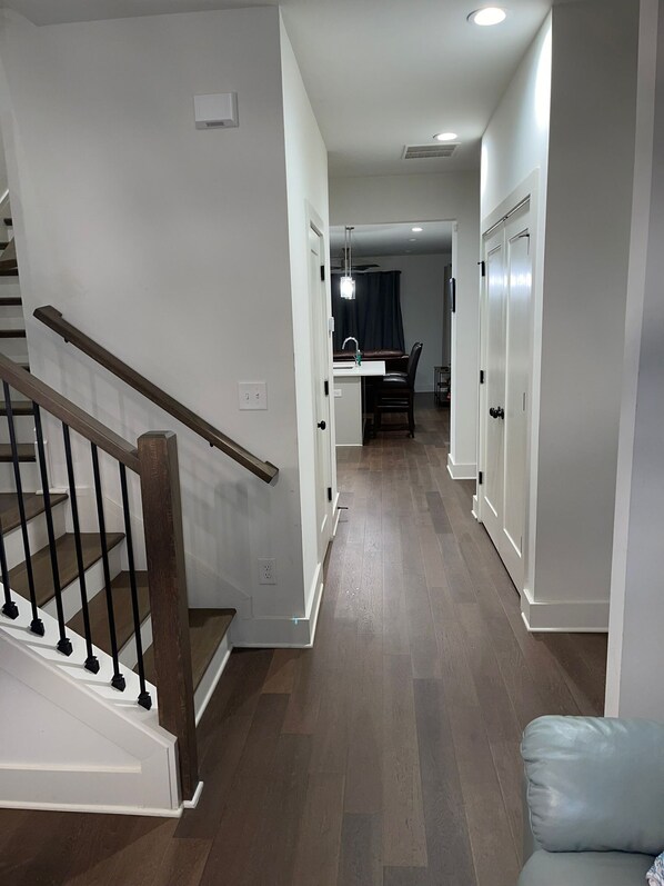 A modern interior with a wooden staircase, a dining area, and a hallway leading to a bedroom.