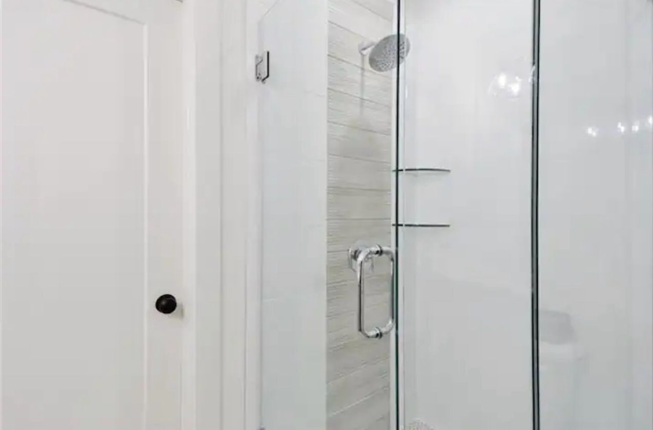Une salle de bain moderne avec une douche à parois de verre, une porte blanche et un porte-serviettes visible.