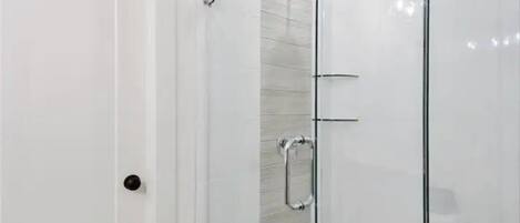 Une salle de bain moderne avec une douche à parois de verre, une porte blanche et un porte-serviettes visible.