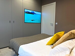 Makuuhuone, jossa on sänky, seinälle asennettu televisio ja ovi.