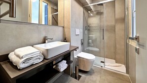 A modern bathroom with a large mirror, a sink, a toilet, and a glass-enclosed shower.