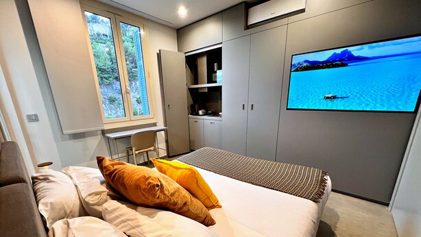 A modern bedroom with a bed, a desk, and a TV displaying a scenic view.