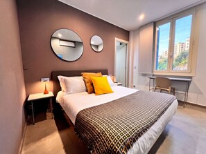 Moderni hotellihuone, jossa on suuri sänky, kaksi yöpöytää, työpöytä ja ikkuna, josta avautuu näkymä kaupunkiin.