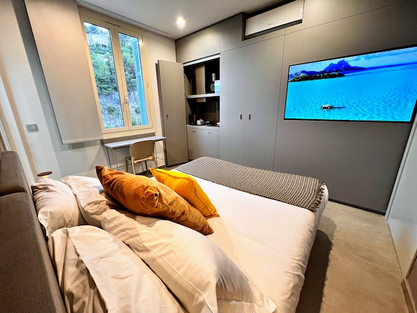 A modern bedroom with a bed, a desk, and a TV displaying a scenic view.