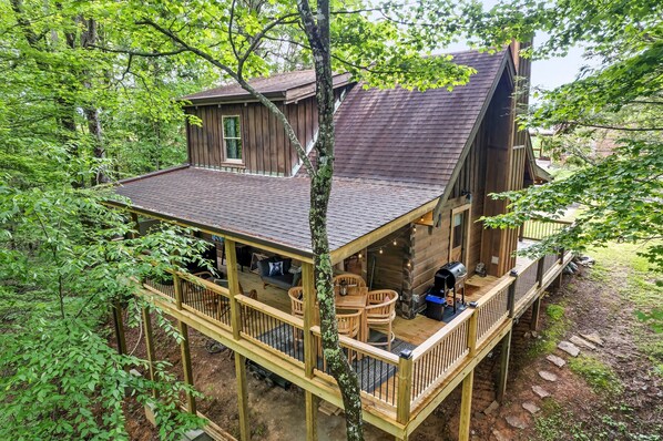 A wooden cabin with a deck, surrounded by trees.