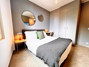 Een moderne slaapkamer met een bed, nachtkastjes, een lamp, een spiegel en een kledingkast.