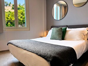 A neatly made bed with a white and gray blanket, a green pillow, and a round mirror on the wall.