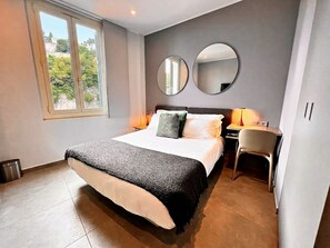 A bedroom with a bed, two round mirrors, a desk, and a chair.