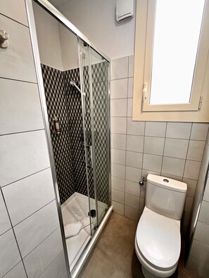 A bathroom with a glass-enclosed shower, a toilet, and a window above the sink.
