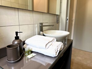 A bathroom with a sink, a mirror, a towel, a soap dispenser, and a glass container.