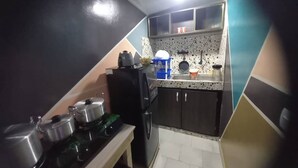 Una cocina compacta con armarios oscuros, una encimera con un hervidor y ollas, y un lavamanos pequeño.