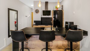 A modern kitchen with a central island, black bar stools, a wooden floor, and a black refrigerator.