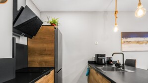 A modern kitchen with black countertops, wooden cabinets, a built-in oven, a coffee maker, and a hanging light fixture.