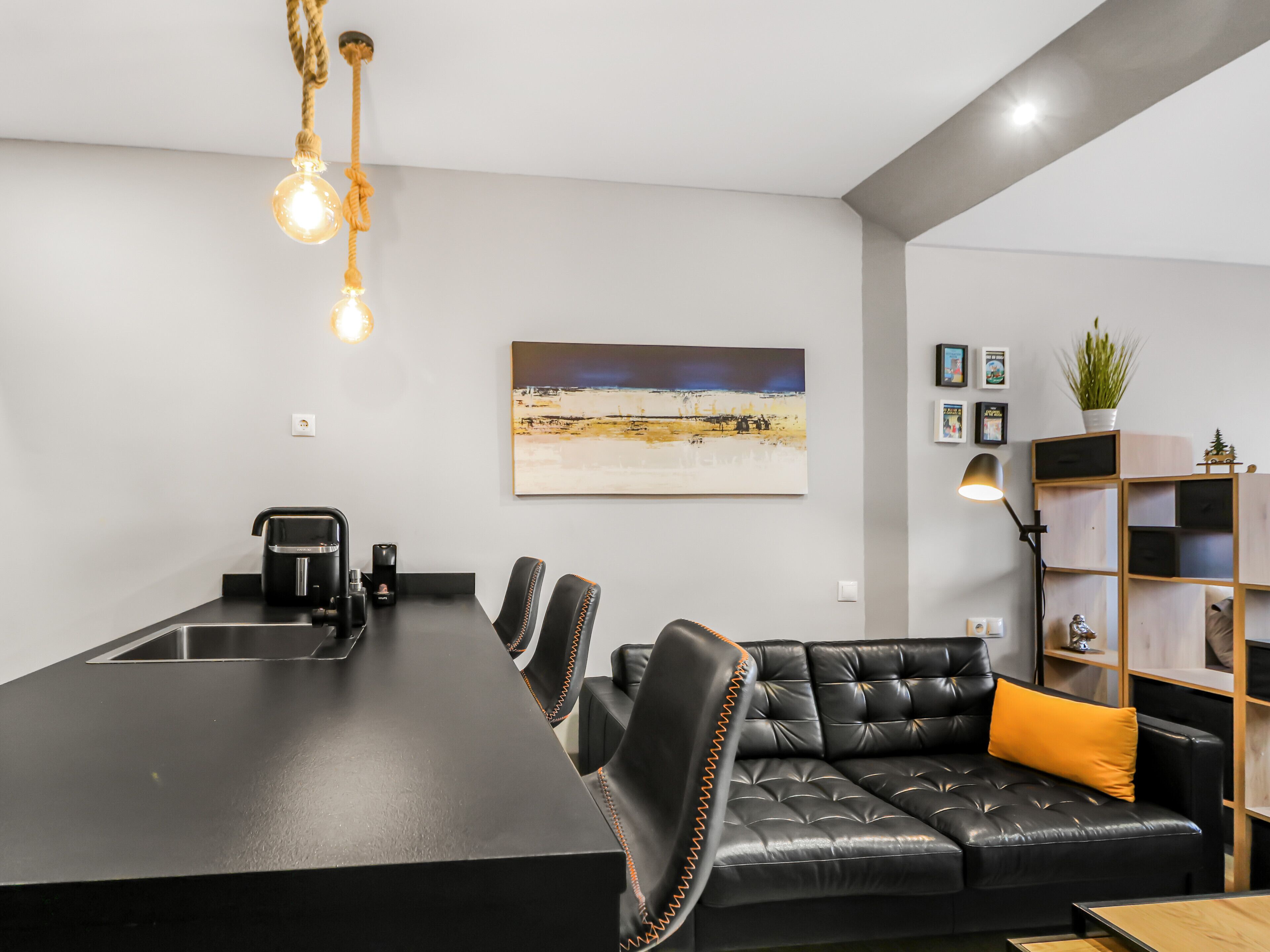 A modern kitchen with a black countertop, a coffee machine, and a seating area with a black leather sofa and a small table.