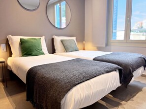 Hotellihuone, jossa on kaksi sänkyä, peili seinällä ja ikkuna, josta on näkymä.