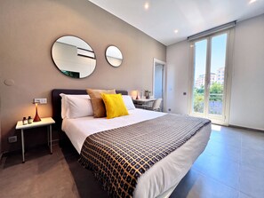 A modern hotel room with a large bed, two bedside tables, a desk, and a balcony with a city view. - MyResidenced'Azur - appartement 7A (Beausoleil)