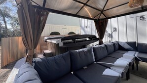 A covered outdoor seating area with a sectional sofa, a grill, and a pergola with a woven light fixture. - Inlet Escape - 5 BR/4 BA House Minutes From Murrells Inlet Marshwalk (Murrells Inlet)