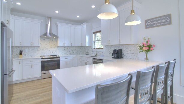 A modern kitchen with white cabinetry, a large island, stainless steel appliances, and pendant lighting. - Inlet Escape - 5 BR/4 BA House Minutes From Murrells Inlet Marshwalk (Murrells Inlet)