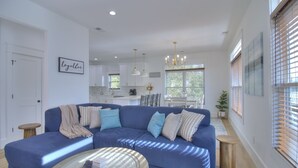 A modern living room with a blue sectional sofa, a round coffee table, and a kitchen in the background. - Inlet Escape - 5 BR/4 BA House Minutes From Murrells Inlet Marshwalk (Murrells Inlet)