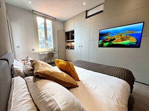 Un dormitorio moderno con una cama, un escritorio y un televisor montado en la pared.
