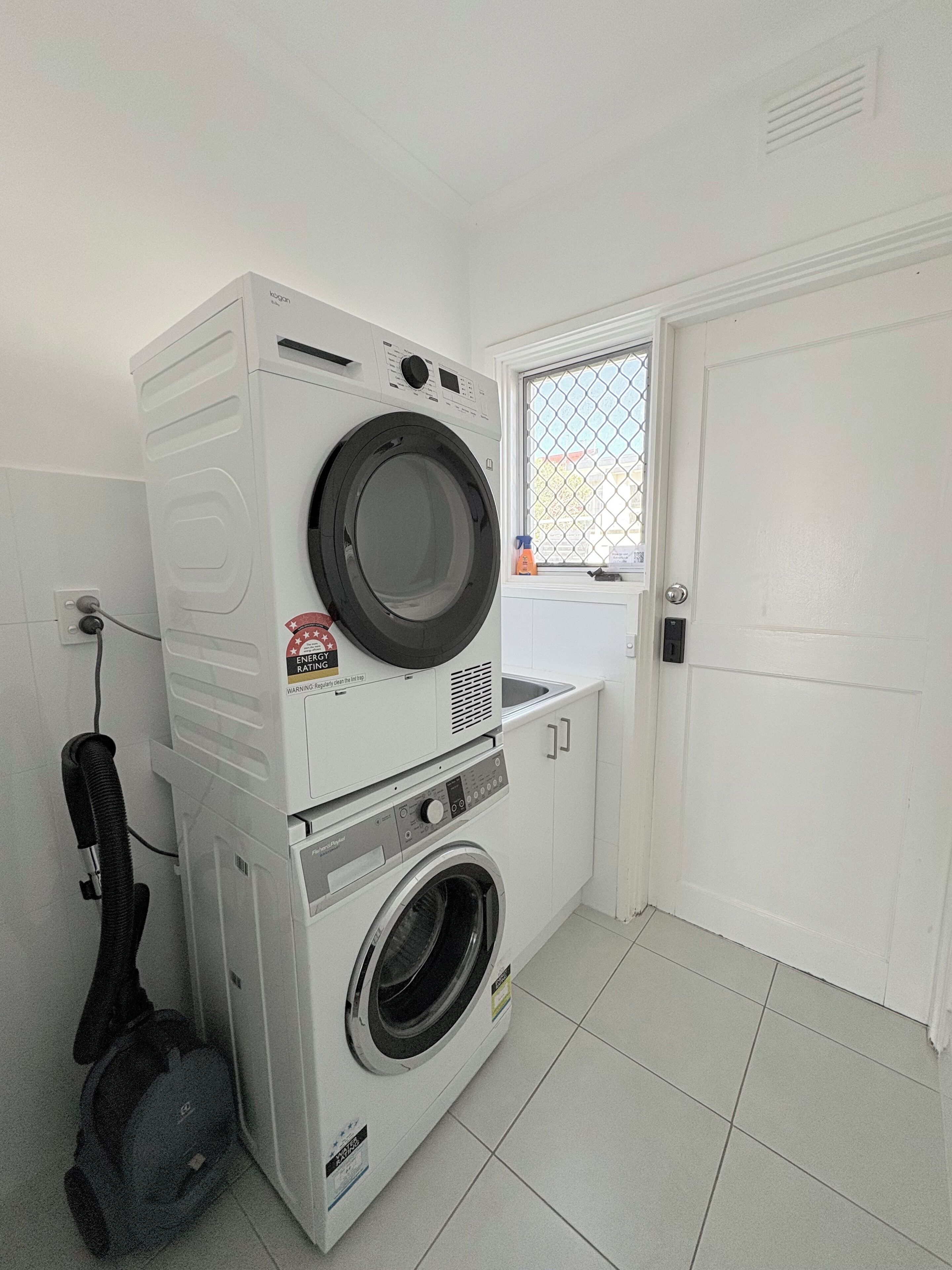 A compact laundry room with stacked washing machines and a dryer, a window with a view, and a door.