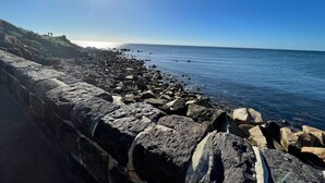 A rocky shoreline with a clear blue sky and the sun shining.