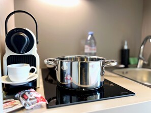 A kitchen with a coffee maker, a pot on an induction cooktop, a cup, and some snacks.