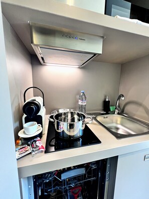 Una kitchenette compacta con cafetera, olla, lavamanos y lavavajillas.