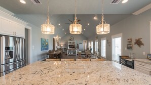 A spacious kitchen with a large granite island, stainless steel appliances, and pendant lighting. - Ocean View | Modern Interior l Tiki Bar l Pet-Friendly (Crystal Beach)