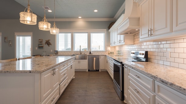 A kitchen with white cabinets, granite countertops, stainless steel appliances, and pendant lighting. - Ocean View | Modern Interior l Tiki Bar l Pet-Friendly (Crystal Beach)
