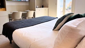 A hotel room with a bed, a desk, a chair, a television, and a window with a city view. - MyResidenced'Azur Maison Micheloni apartment 10A (Beausoleil)