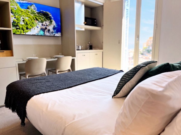 Une chambre d’hôtel équipée d’un lit, d’un bureau, d’une chaise, d’une télévision et d’une fenêtre donnant sur la ville.