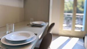 A dining table with plates and a glass, a chair, and a view of an outdoor area through a window. - MyResidenced'Azur Maison Micheloni apartment 10A (Beausoleil)