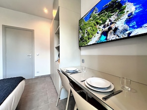 A modern kitchen with a dining area, a flat-screen TV mounted above the counter, and a door leading to another room.