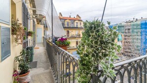A balcony with potted plants, a white cloth, and a view of neighboring buildings.