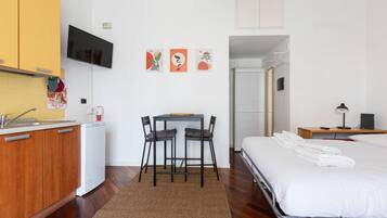 Une chambre d’hôtel comprenant un lit, un bureau avec une chaise, une petite kitchenette et un téléviseur fixé au mur.