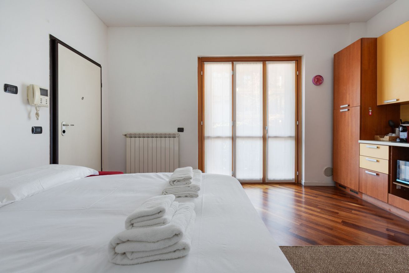 Una camera d'albergo con un letto, un armadio in legno, un termosifone e una porta scorrevole in vetro.