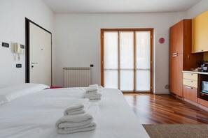 A hotel room with a bed, a wooden wardrobe, a radiator, and a sliding glass door.