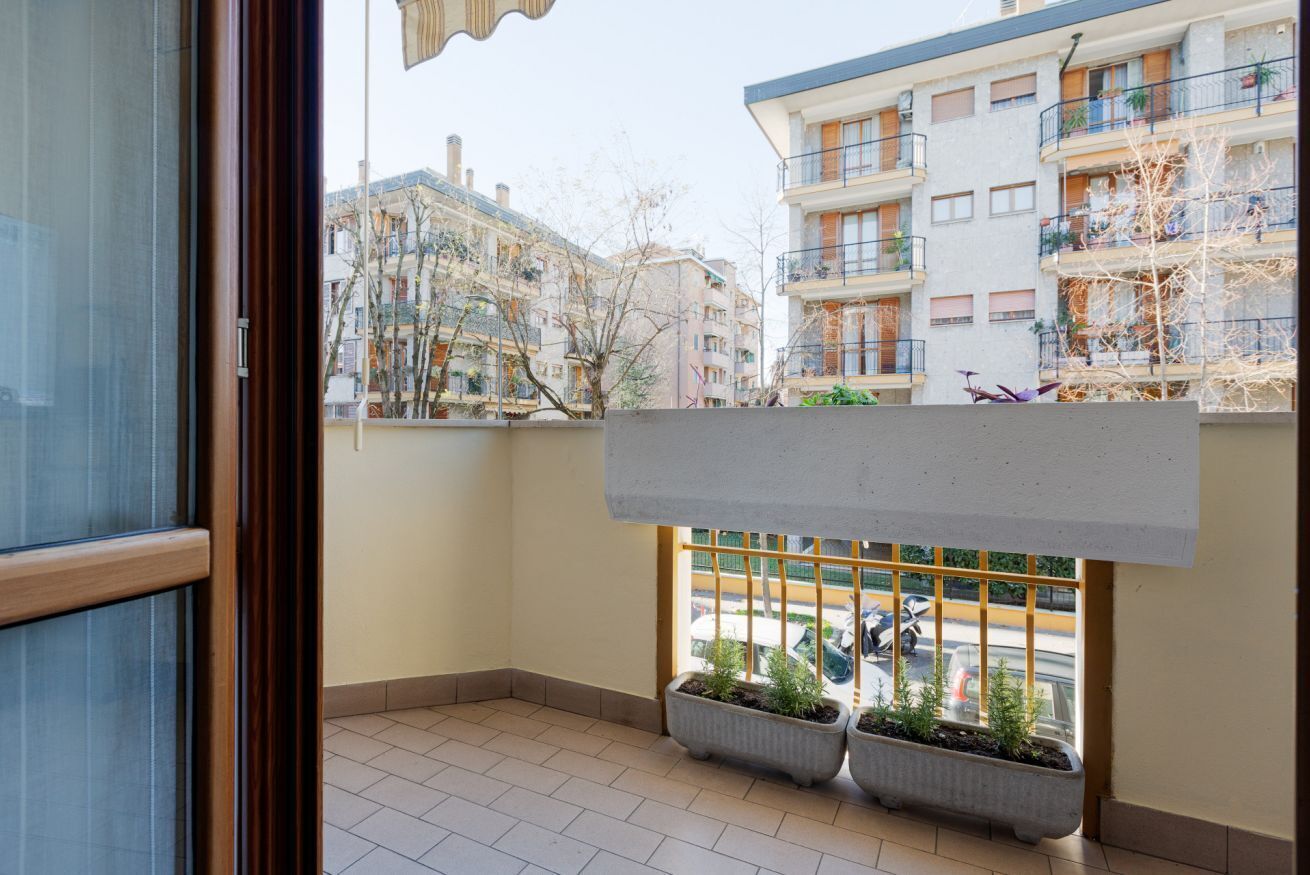 A balcony with potted plants, a view of neighboring buildings, and a clear sky.