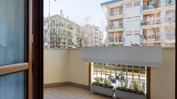 Un balcon agrémenté de plantes en pot, une vue sur les immeubles voisins et un ciel dégagé.